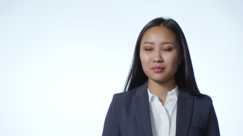 Young asian businesswoman holding hundred renminbi bills fan, getting excited, covering mouth with hand and smiling at camera while posing against white background in studio