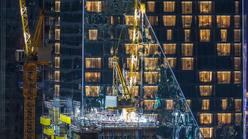 Construction site with cranes  night timelapse. Building of skyscrapers. Aerial top view with many workers and glowing windows on background Royalty-Free Stock Footage #1023183631
