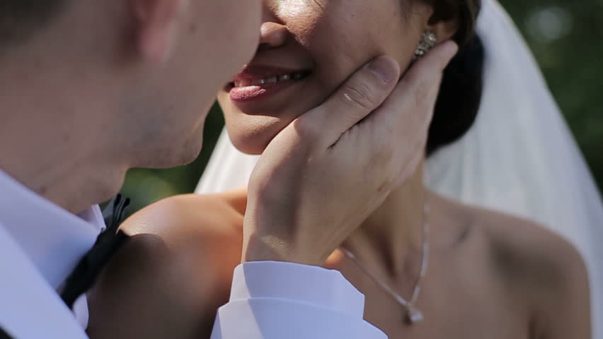 Young asisn bride and groom are kissing in a sunny park