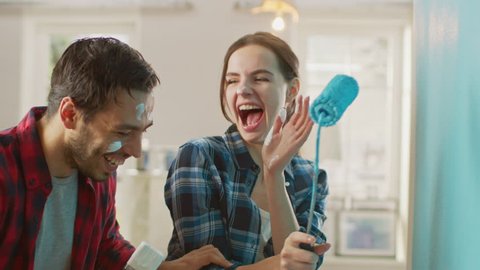 Beautiful Couple Decorate Their New Apartment and Fool Around. Husband and Wife are Painting the Wall with Rollers that are Dipped in Light Blue Paint. They are Happy and Have Fun. Renovations at Home
