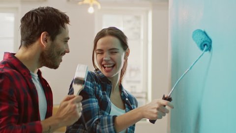 Beautiful Couple Decorate Their New Apartment and Fool Around. Husband and Wife are Painting the Wall with Rollers that are Dipped in Light Blue Paint. They are Happy and Have Fun. Renovations at Home
