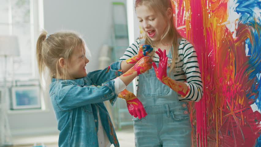 Two Fun Little Sisters Play and Fool Around with Their Hands Dipped in Colorful Paint. They are Happy and Laugh. Sisterhood Goals. Redecoration at Home. Royalty-Free Stock Footage #1023188065