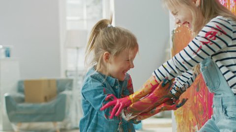 Two Fun Little Sisters Play and Fool Around with Their Hands Dipped in Colorful Paint. They are Happy and Laugh. Sisterhood Goals. Redecoration at Home.