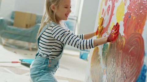 Happy Little Girl Dips Her Hands in Paint and Starts Painting Handprints on the Wall. She is Having Fun and Laughs. Home is Being Renovated.