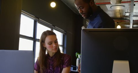 Front view close up of young Caucasian businesswoman working on laptop at desk in a modern office. African american businessman enters and discussing with businesswoman over digital tablet