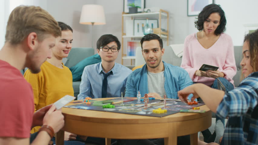 Diverse Group of Guys and Girls Playing in a Strategic Board Game with Cards and Dice. Cozy Living Room in a Daytime Royalty-Free Stock Footage #1023193114