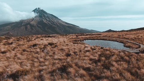 Dramatic drone aerial footage of Mount Taranaki Egmont National Park 4k flying forwards and low over 2 hikers