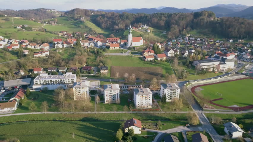 Aerial: Flying over catholic church with big parking place beside. Filming small village on beautiful spring sunny day.
