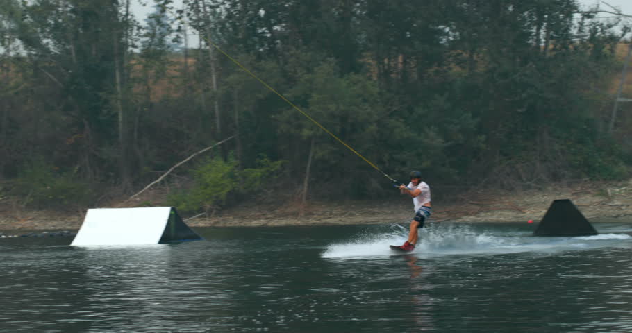  Front view of young Caucasian man doing tricks on wakeboard in the city lake. Rider holding wakeboard rope 