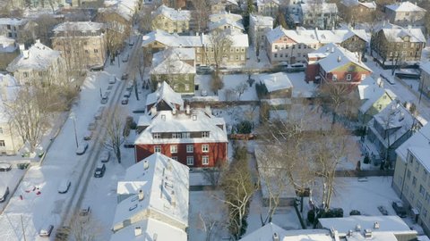 Aerial over small and old snowy suburb neighborhood in Europe. Slow aerial winter shot of colorful wooden buildings with rooftops covered in snow.