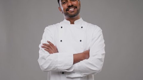 cooking, profession and people concept - happy male indian chef in white jacket over grey background