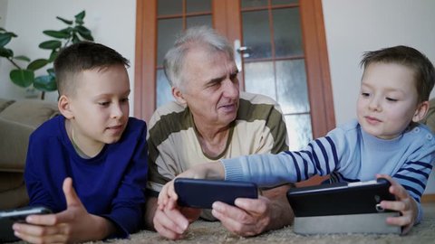 Granddad and grandchildren play on tablet in internet game in room. Home education. Fun pastime.