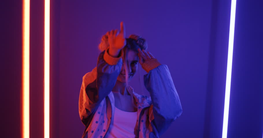 Portrait shot of the young blond stylish Caucasian girl posing to the camera on the pink and violet neon light background.