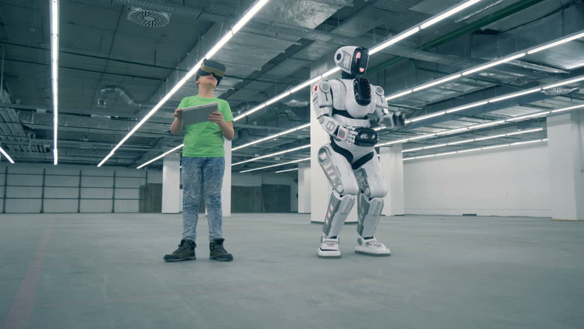 Boy in VR-glasses with a tablet and a robot moving near him