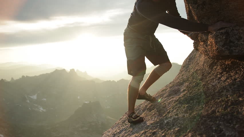 Legs of a man climbing a rock at sunset.