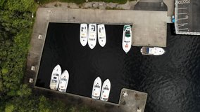 Aerial footage (birds-eye view) of boats berthed in a small marina on black water.