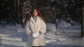 Young woman throws up snow in winter forest sunny day and laughing