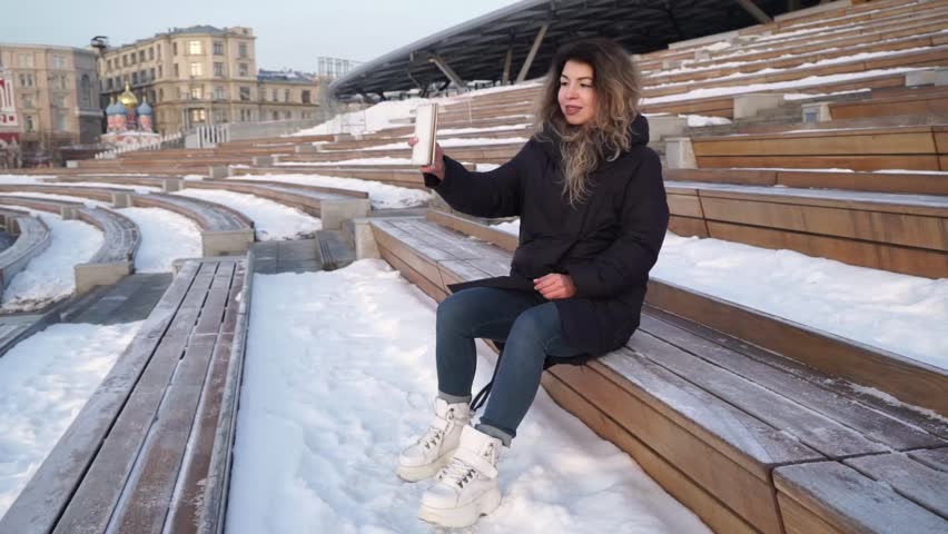 Beautiful teen girl making safe on phone does smile at winter park. Selfi on phone.