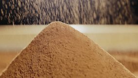 Close-up of sifting cocoa powder sieve. Cocoa powder in slow motion falls on a hill of cocoa powder on a wooden table.