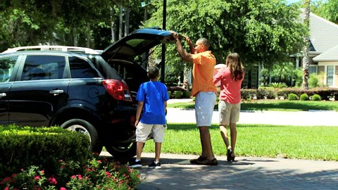Happy young African American parents son getting into family car for day out together