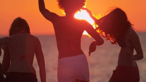 Carefree male female teenagers enjoying spring break together having fun on beach at sunset in silhouette slow motion shot on RED EPIC