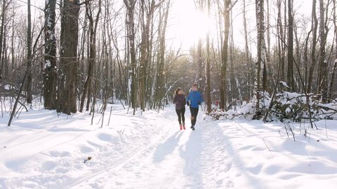 Winter forest. Young man and woman running in the morning woods. People skiing on the background