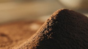 Close-up of sifting cocoa powder sieve. Cocoa powder in slow motion falls on a hill of cocoa powder on a wooden table on a brown background