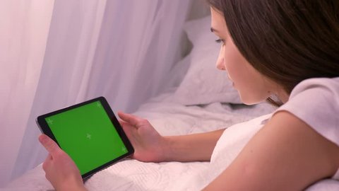 Closeup portrat of young caucasian female laughing while playing video on the tablet with green chroma-key screen indoors