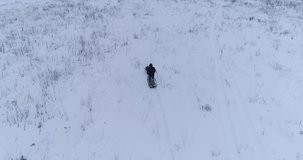 Video of the man rides on a snow-covered field on a snowmobile. Drone video of the snowmobile driving by winter field and forest. Aerial footage.