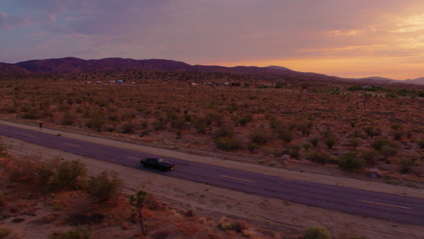Epic sunset in desert with Classic 1969 Camaro driving down empty road - Aerial 4K Royalty-Free Stock Footage #1023296992