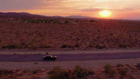 Epic sunset in desert with Classic 1969 Camaro driving down empty road - Aerial 4K