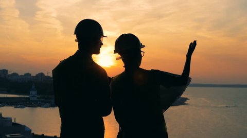 Workers talk, standing on a sunset background, back view.