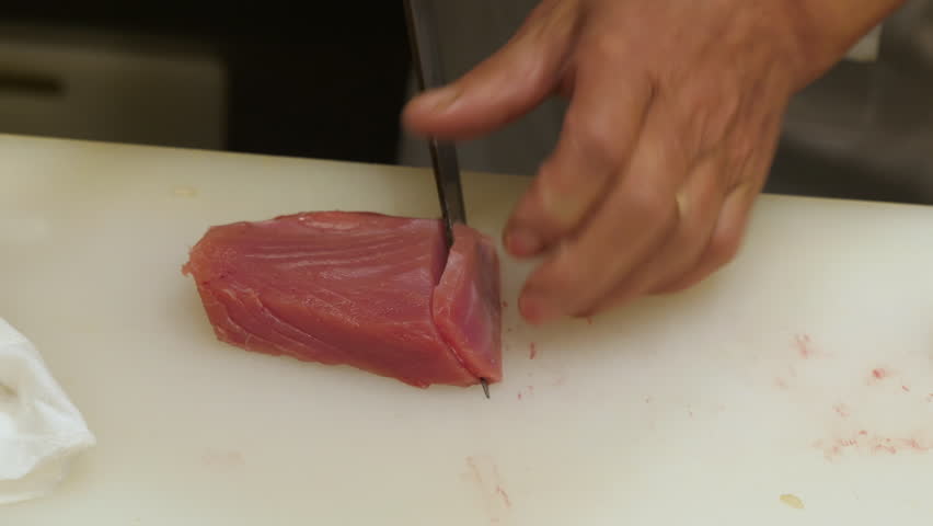 Japanese food: Close-up of sushi chef slices fresh tuna at sushi bar