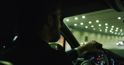 Slow motion of young handsome businessman driving a modern car in center of the city by night. Shot in 8K. Concept of business, success, traveling, luxury