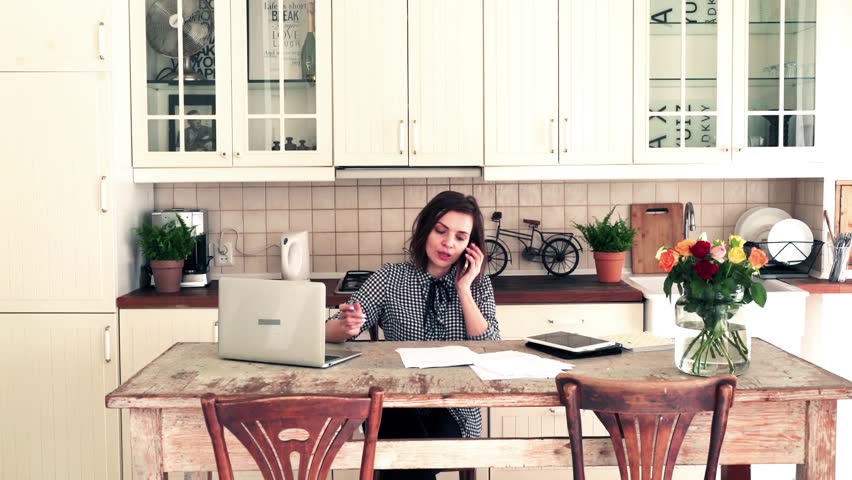 Pretty businesswoman talking on cellphone and working on laptop at home
