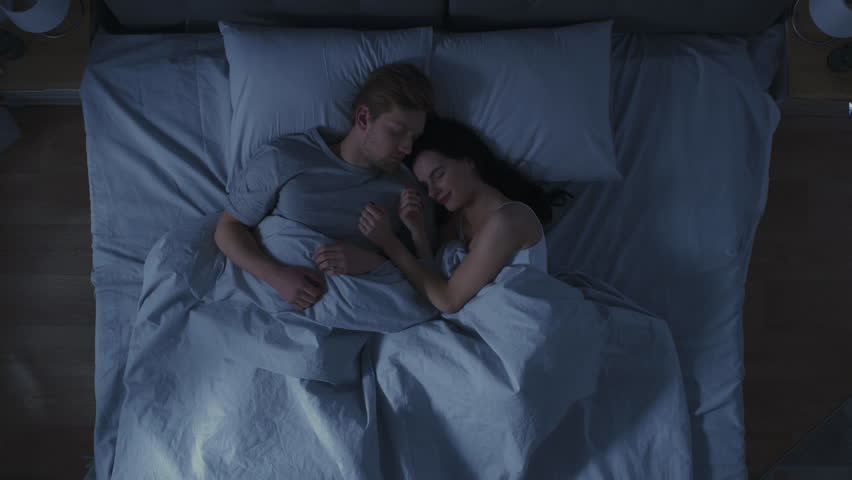 Happy Young Couple Cuddling Together in the Bed Sleeping at Night. Beautiful Girl and Handsome Boy Sleeping Together, Sweetly Embracing Each other. Top Down Shot | Shutterstock HD Video #1023333721