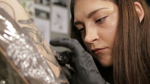 Caucasian Female tattoo artist in process of work, close-up view on focused face