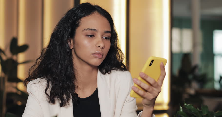 Tired business woman using smartphone in cafe. Girl sitting in modern coworking and drinkin