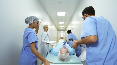 Following dolly shot of emergency room doctor and nurses administering oxygen and IV fluids to patient while running and pushing gurney along hospital corridor