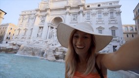 Young woman taking selfie portrait at the Trevi fountain in Rome, Italy ; Caucasian female capturing selfie with mobile phone at famous place in Capital city in Europe 