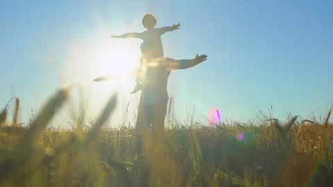 silhouette of father and son playing, airplane arms raised at sunset in wheat field, happy family children flying outdoors. child little boy having fun, rising up hands, travel, holiday nature summer
