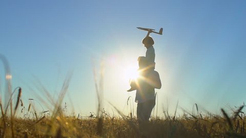 silhouette of happy father and son playing with airplane toy together at sunset in wheat field nature summer day. happy family walking outdoors. child boy having fun, aircraft flying in sky flight