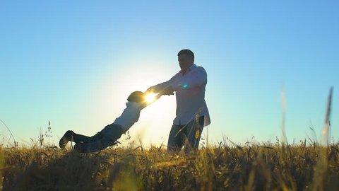 silhouette of father and son playing and enjoying sunset in wheat field in nature on summer day. happy family walking outdoors, having fun. father circling children child little boy by taking hands