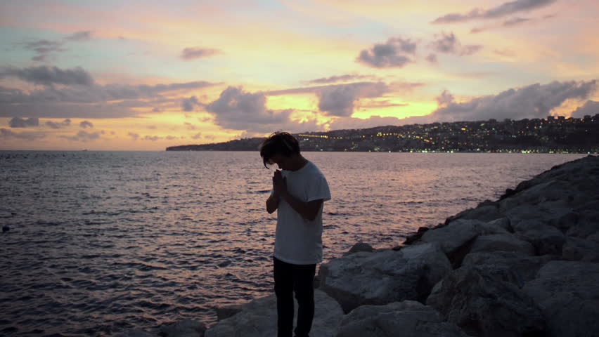 Guy stands on the stones and look at the sunset slow motion