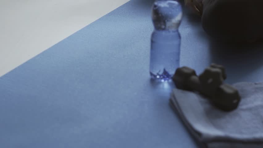 Young fit woman exercising at home, she is sitting on the mat and drinking water, fitness and wellness concept