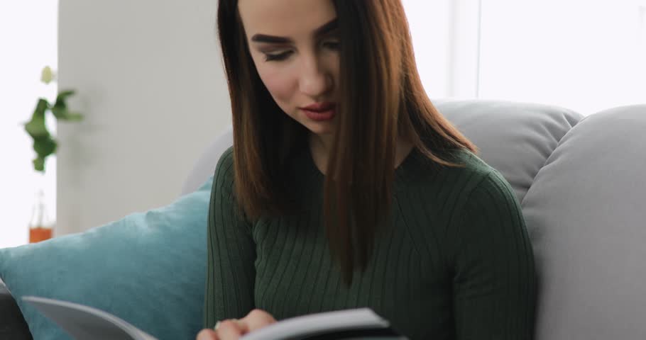 Woman reading book at home sitting on a comfortable sofa at the rest day