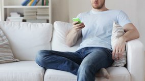 technology, people, lifestyle and communication concept - close up of man with smartphone texting message and sitting on couch at home
