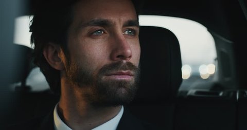 Slow motion close up of young handsome businessman looking outside during traveling in a modern car with a driver in center of the city by day.Shot in 8K.Concept of business,success, traveling luxury 