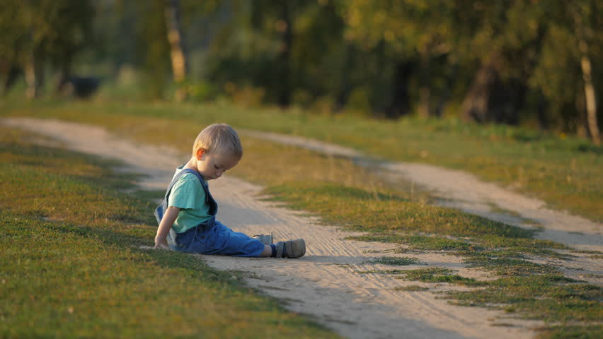 Funny single baby child sitting on the countryside path and p[lay with dust, kid feel the joy of ground, magic sunset light