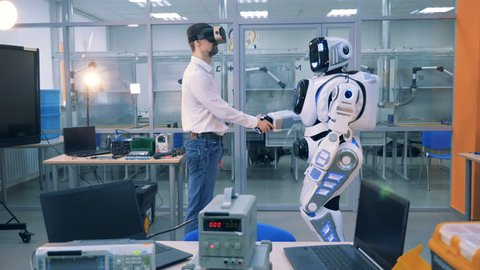 An engineer in augmented reality glasses and a robot are shaking hands 